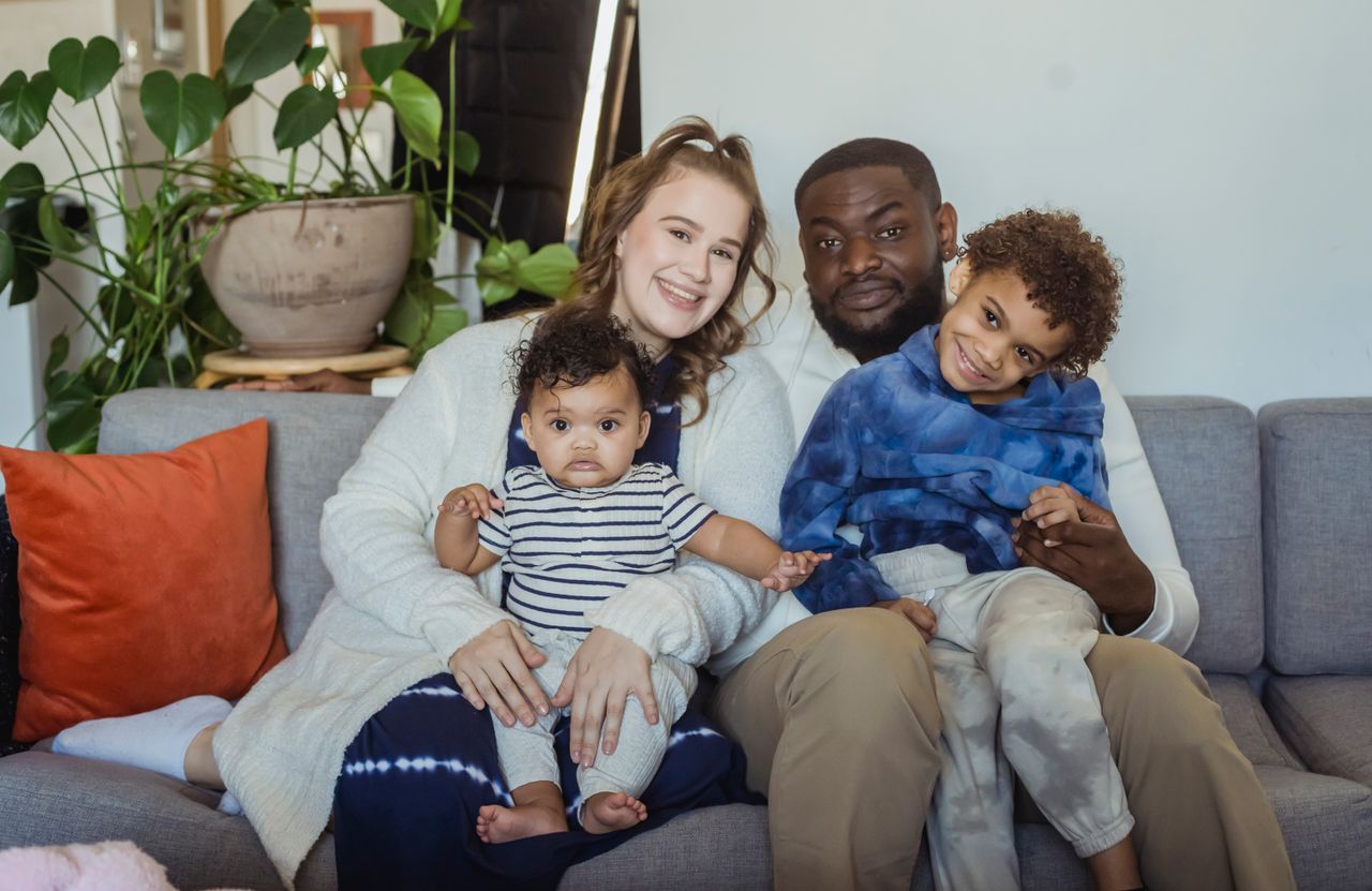 Joyful family portrait of parents with two young children sitting together on a cozy sofa.