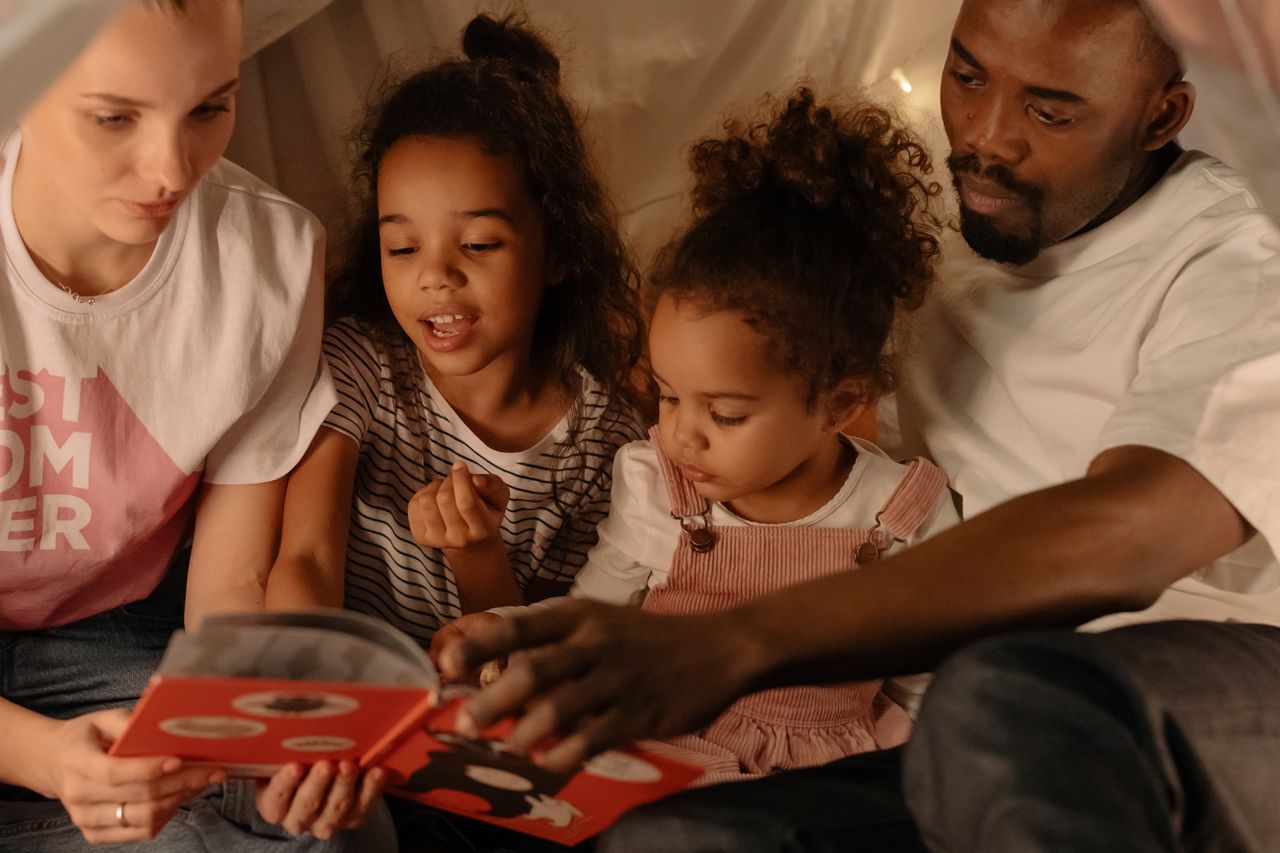 A diverse family of four reading a book together in a cozy indoor tent.