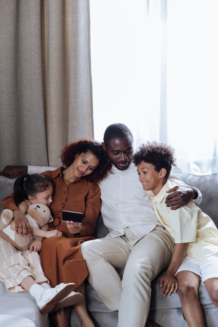 A loving family of four sitting on a couch indoors sharing a joyful moment.